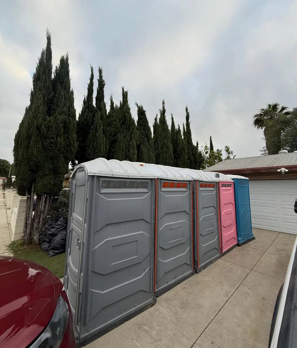 Standard porta potties lined up along a fence for a work crew