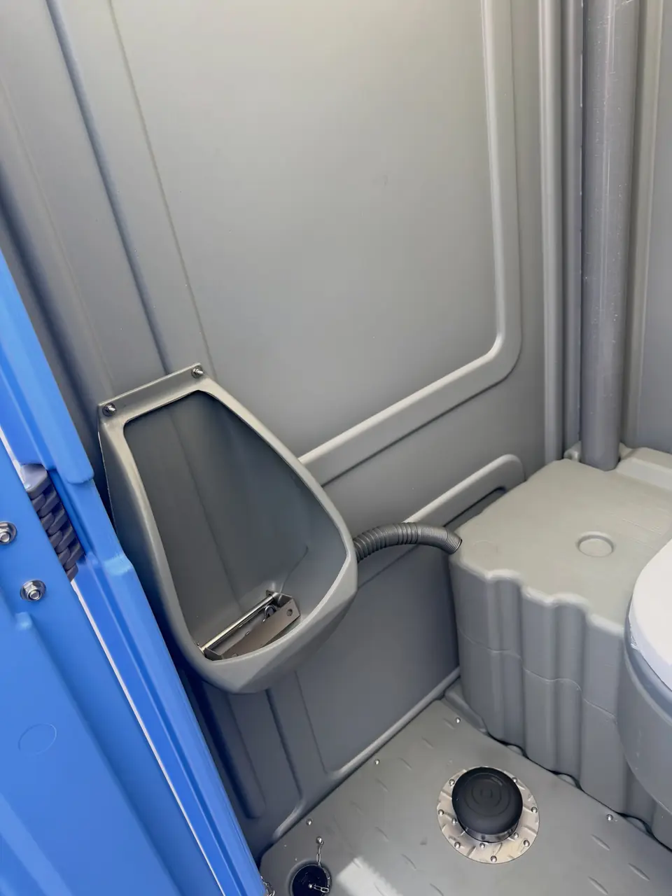 Inside a standard porta potty showing the urinal and wall vent