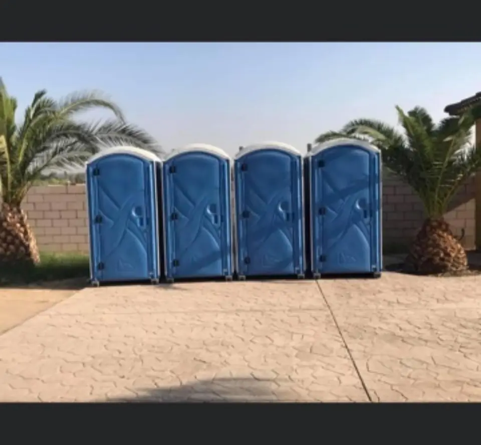 Four standard porta potties lined up on a paved lot