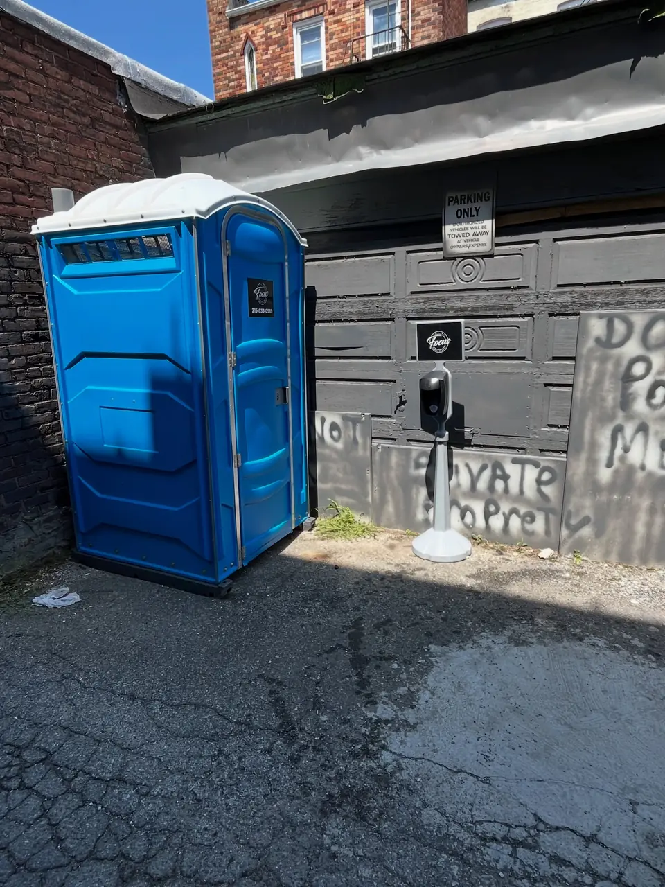 Blue porta potty placed on a paved spot beside a building